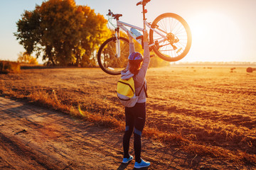Young bicyclist raising her bicycle in autumn field. Happy woman celebrates victory holding bike in...
