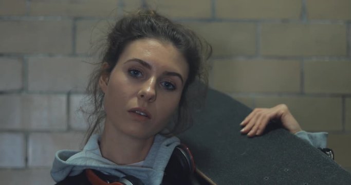 Girl standing in underpass at night. Young caucasian woman with skateboard in dark underground tunnel. Urban city lifestyle. 4k video shooting by handheld gimbal
