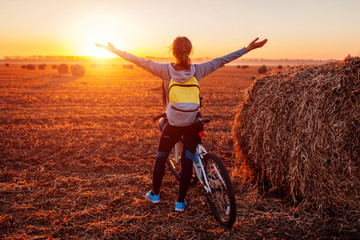 Happy young bicyclist raising opened arms in autumn field admiring the view. Woman riched...