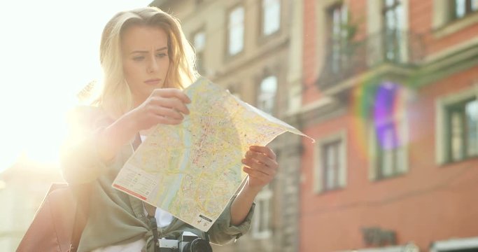 Young attractive woman tourist standing with a map and looking for a place to go on it in the new city while travelling.
