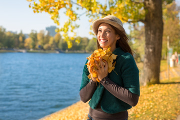 Beautiful young woman holding autumn leaves in her hand while smiling