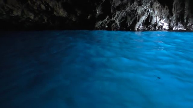 Shiny vivid blue water and stone wall view from boat inside the cave