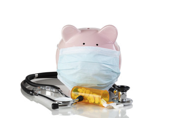 Piggy bank wearing surgical mask with medical drug supplies isolated on a white background