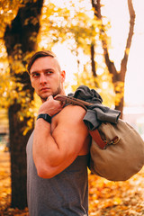 A handsome man stands in an autumn park in sportswear.