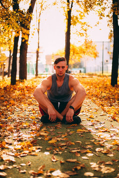 Handsome man squatting in autumn park in sportswear.