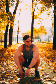 Handsome man squatting in autumn park in sportswear.