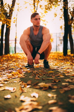 Handsome man squatting in autumn park in sportswear.