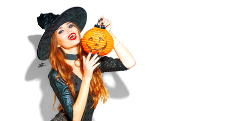 Halloween. Sexy witch with bright holiday makeup. Beautiful young woman posing in witches costume with pumpkin lantern over white background