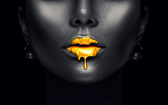 Fototapeta Złota farba kapie z seksownych ust, złote krople cieczy na ustach pięknej modelki, kreatywny abstrakcyjny makijaż w kolorze ciemnej czerni. Piękno kobiety twarz odizolowywająca na czerni