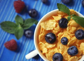 Healthy eating, food and diet concept - Cornflakes with berries raspberries and blueberries on blue wooden background. Top view.
