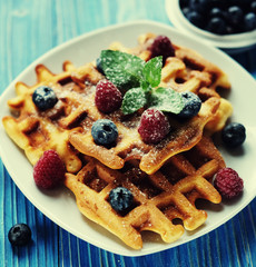 Belgian waffles with blueberries, raspberries and powdered sugar on wooden table.