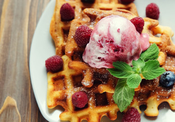 Plate of belgian waffles with ice cream and fresh berries - raspberries and blueberries.