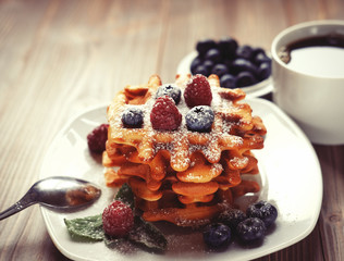 Waffles with  berries on a white plate and coffee, close up.