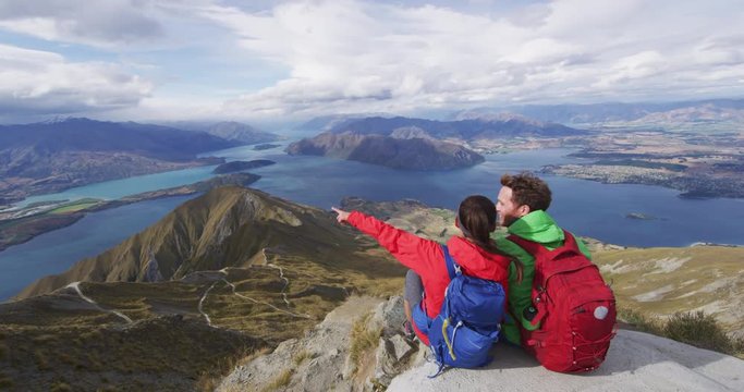 Wanderlust adventure and hiking travel vacation concept with hikers relaxing looking at view. Hiking couple tramping up famous hike to Roys Peak on South Island, New Zealand. SLOW MOTION.