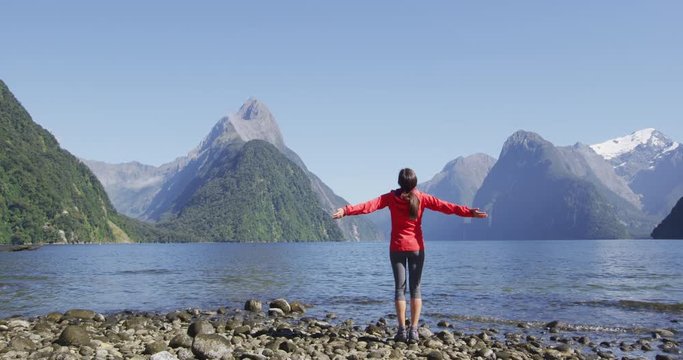 Harmony with nature - happy free woman with wanderlust enjoying Milford Sound hiking in New Zealand enjoying iconic view of Mitre Peak, Fjord and famous tourist destination in Fiordland National Park,