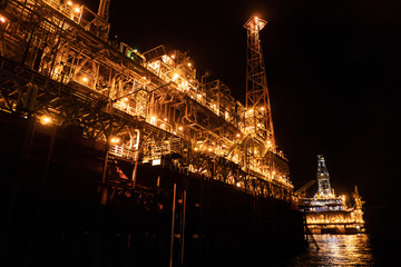FPSO tanker vessel near Oil platform Rig. Offshore oil and gas industry, sea oil production and storage. Flare boom is brightly burning at night.