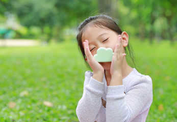 Adorable little Asian child girl smelling food in her hands at green grass garden.