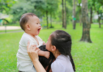 Happy baby boy riding on mom's shoulder playing with sister in the nature park.
