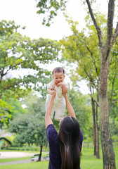 Asian mother throws up happy infant baby boy in arms at garden.