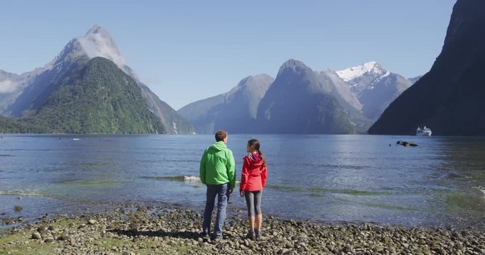 New Zealand - tourist couple hiking looking at Milford Sound enjoying iconic view and famous tourist destination in Fiordland National Park, South Island, New Zealand. Couple embracing. SLOW MOTION.