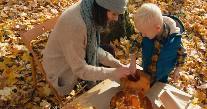 Caucasian family - mother and son, carving pumpkins for Halloween on the table outdoors in the backyard. 4K UHD 60 FPS