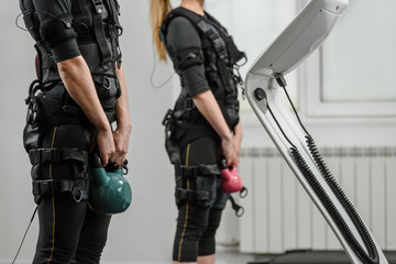 Closeup of two women in EMS suits doing exercises with kettlebell