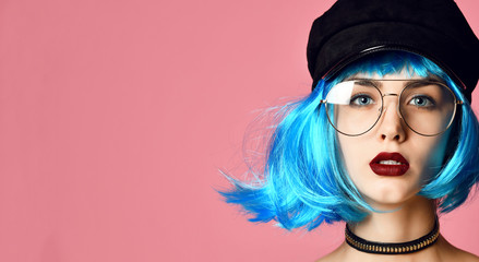 Young grunge style woman with blue wig hair in gold chain choker on neck and black leather hat