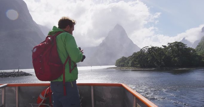 Travel photographer tourist taking photo of Milford Sound and Mitre Peak in Fiordland National Park, New Zealand while on cruise ship boat tour.