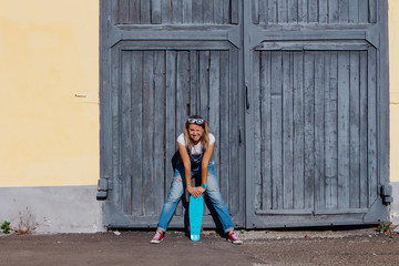 Portrait of a smiling woman standing with her skateboard next to the old wooden wall.