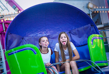 Two cute teen girls playing and having fun while riding an amusement park ride. Sticking out their tongues at pulling a funny face. Carefree and fun-loving teen girls at a carnival