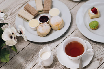 Traditional English afternoon tea: scones with clotted cream and jam, strawberries, with various sandwiches on the background