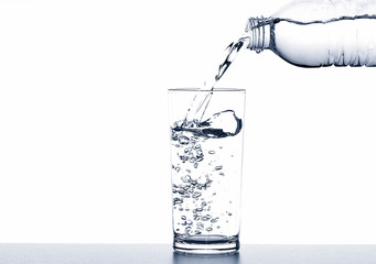 Pouring drinking water from bottle into glass on white background