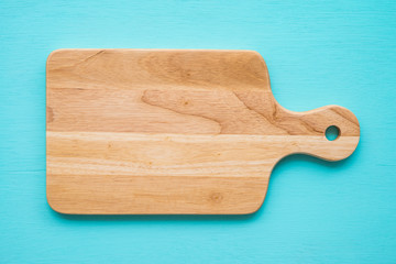 Top view of unused brand new brown handmade wooden cutting board on blue wooden table background