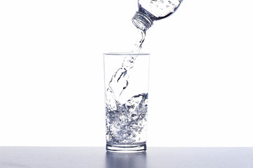 Pouring drinking water from bottle into glass on white background