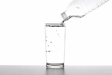 Pouring drinking water from bottle into glass on white background