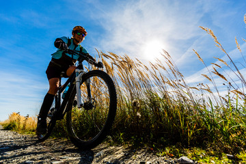 Naklejka na ściany i meble Cycling, mountain bikeing woman on cycle trail in autumn forest. Mountain biking in autumn landscape forest. Woman cycling MTB flow uphill trail.