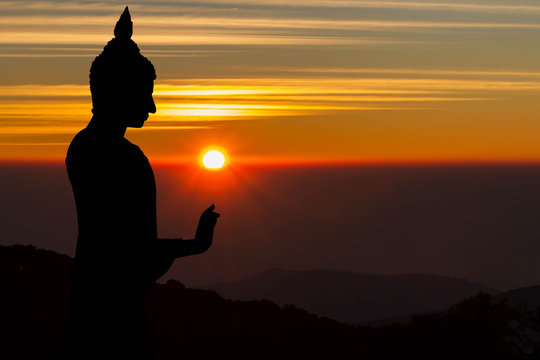 Silhouette of Buddha statue on blurred golden sunrise background