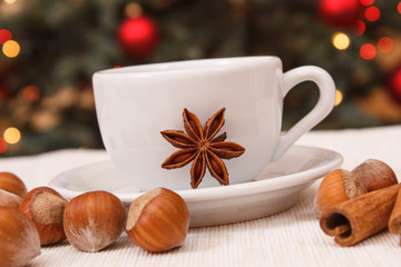 Obraz na płótnie Canvas Hazelnuts, spices, cup of coffee or tea and christmas tree with lights in background
