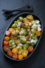 Roasted brussels sprouts served with cherry tomatoes and grated cheese in a cast-iron pan, selective focus