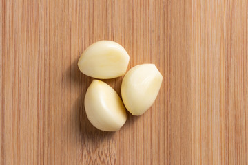 Peeled garlic on wooden plate in the middle. Top view