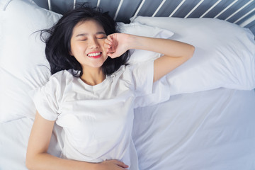 Woman stretching in bed after waking up, back view. Woman sitting near the big white window while stretching on bed after waking up with sunrise at morning, back view.