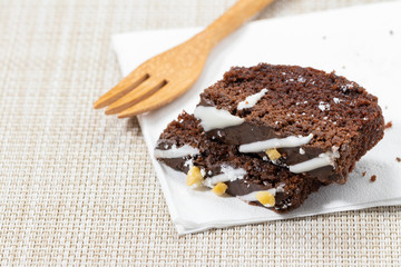 Two chocolate brownies on a white paper. And there is a spoon on the side.