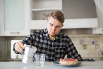 People, breakfast and drinks concept - handsome bearded young man is drinking coffee in kitchen