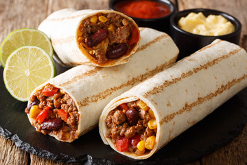 Mexican grilled burrito with beef and vegetables served with sauces close-up. horizontal