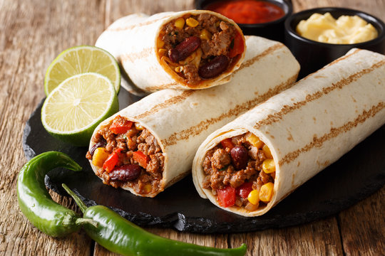 Fresh hot grilled burritos with minced beef, beans, corn, pepper and tomatoes and with sauces close-up. horizontal