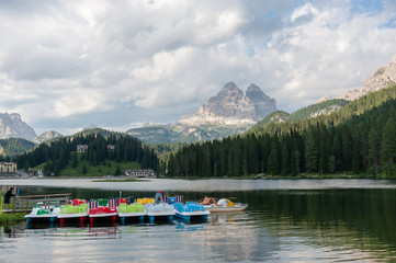 Fototapeta na wymiar Elderly couple tending to the boats, at the end of a summer's day, on lake Misurina, in the Italian Alps, surrounded by imposing mountains. Italian Dolomites, summer of 2018.