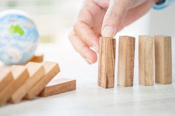Strategy planning risk in business concept : Businessman or engineer placing wooden block dominos on table with blur global model. Alternative risk for goal and success