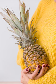 Closeup of juicy pineapple in girl's hands against the background of a yellow sweater. Healthy food concept
