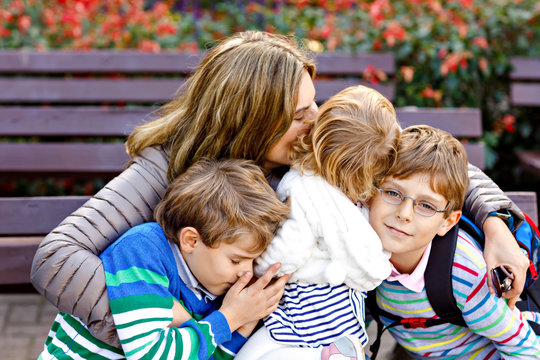 Mother and three children hugging. Happy family sitting outdoor: woman and two brother kids boys and cute little toddler girl. Siblings and mum in love
