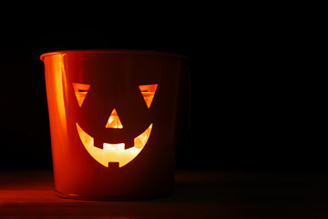 Halloween Jack o lantern with glowing face on black background, isolated. Glowing spooky funny face on bucket in dark. Space for text. Mockup for halloween. Trick or treat